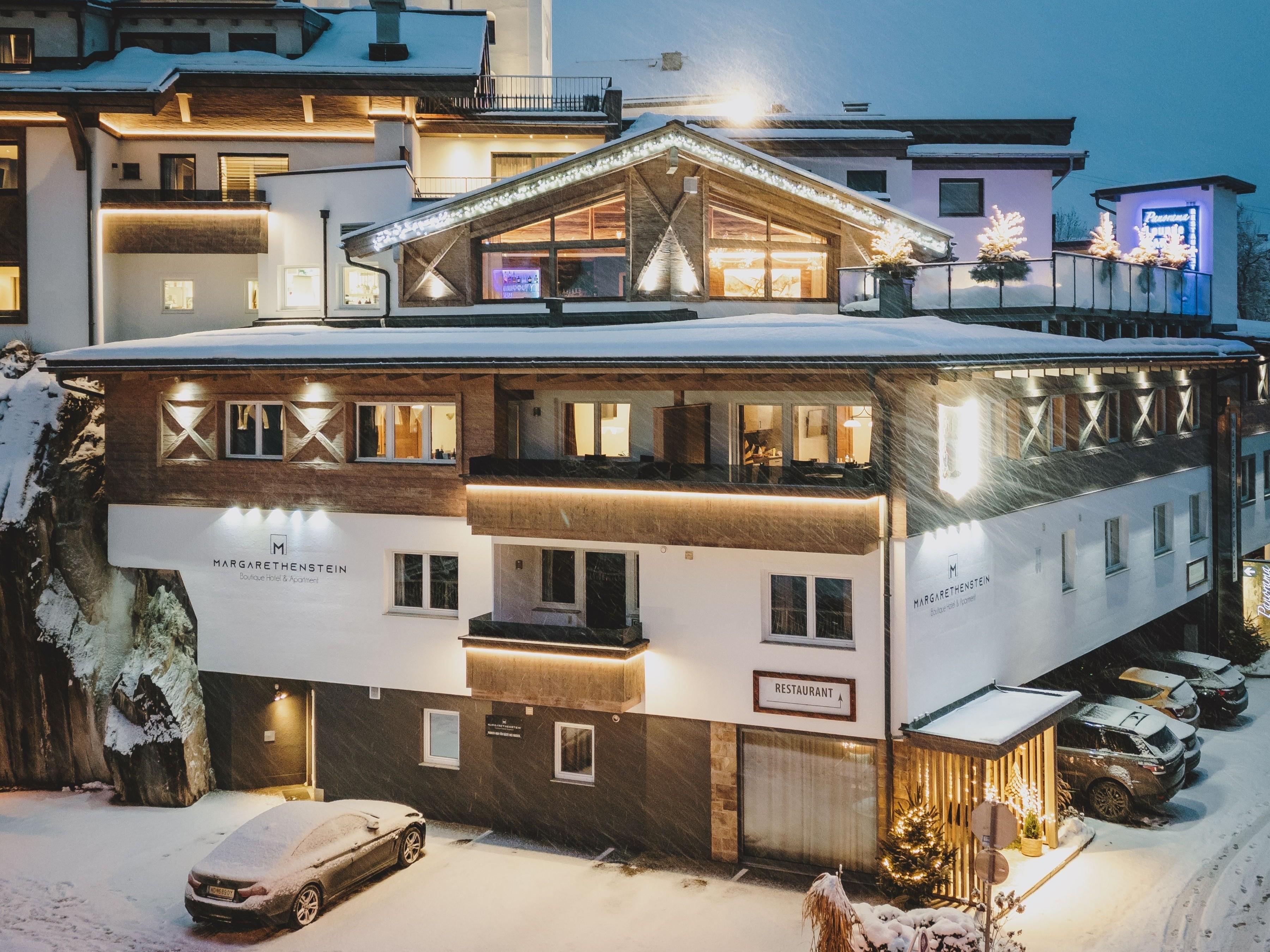 Eine beeindruckende Burg im Schnee, umgeben von Bäumen und einem kleinen Dorf. Die Landschaft ist ruhig und nachts beleuchtet.