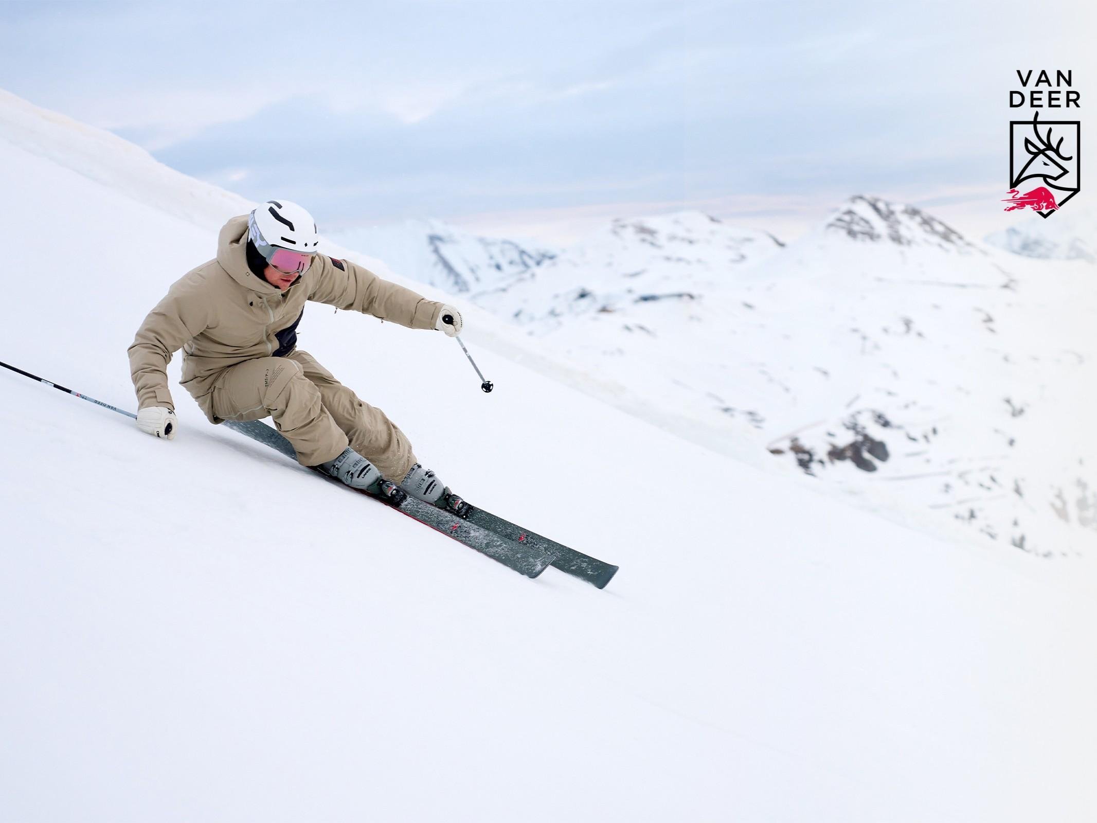 Eine Snowboarderin fährt geschmeidig auf einer schneebedeckten Piste. Im Hintergrund sind Zuschauer und eine Rampe zu sehen.