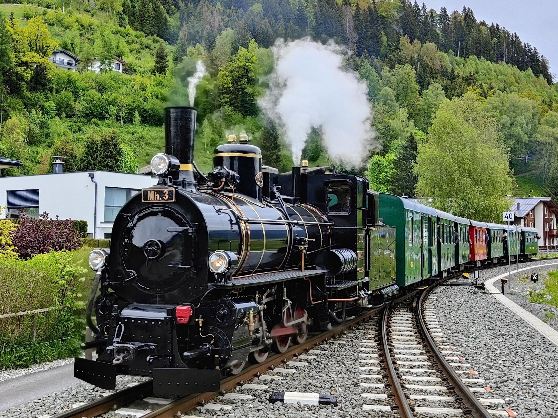 Eine bunte Lokomotive steht neben einem Waggon auf den Gleisen. Der klare Nachthimmel mit einem großen Mond und vielen Sternen ist im Hintergrund zu sehen.