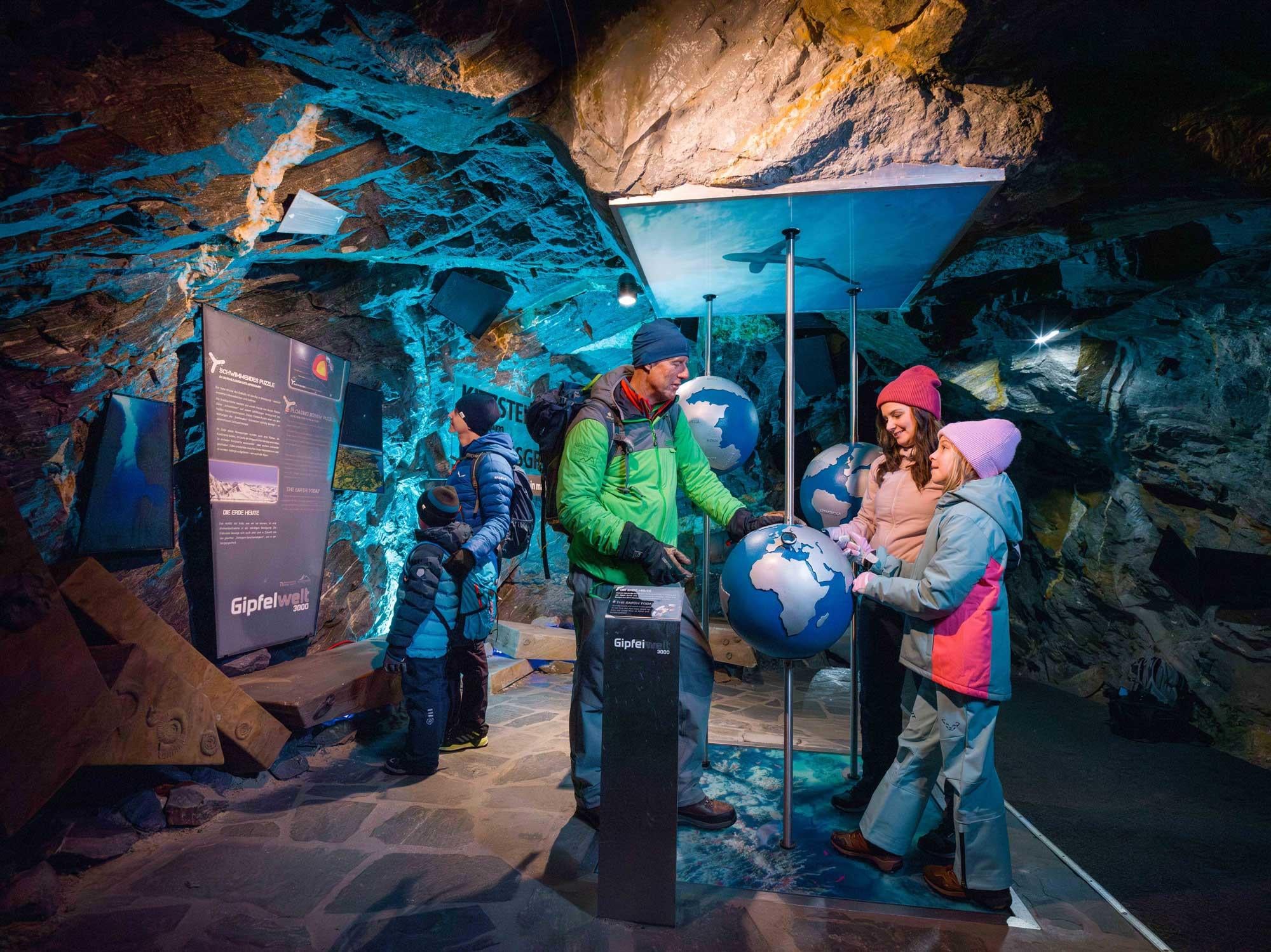Eine Gruppe von Menschen erkundet eine Ausstellung in einer Höhle. Sie betrachten interaktive Globusmodelle und Informationen an den Wänden.