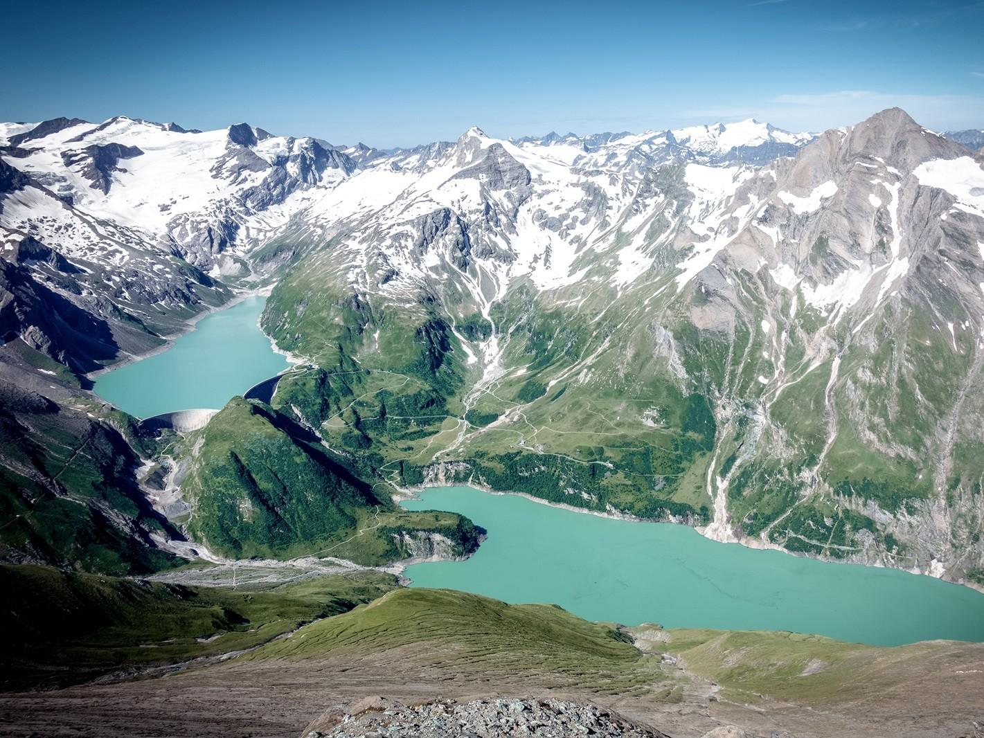 Eine beeindruckende Berglandschaft mit schneebedeckten Gipfeln und smaragdgrünem Wasser. Die Aussicht zeigt einen klaren Himmel und üppige grüne Täler.