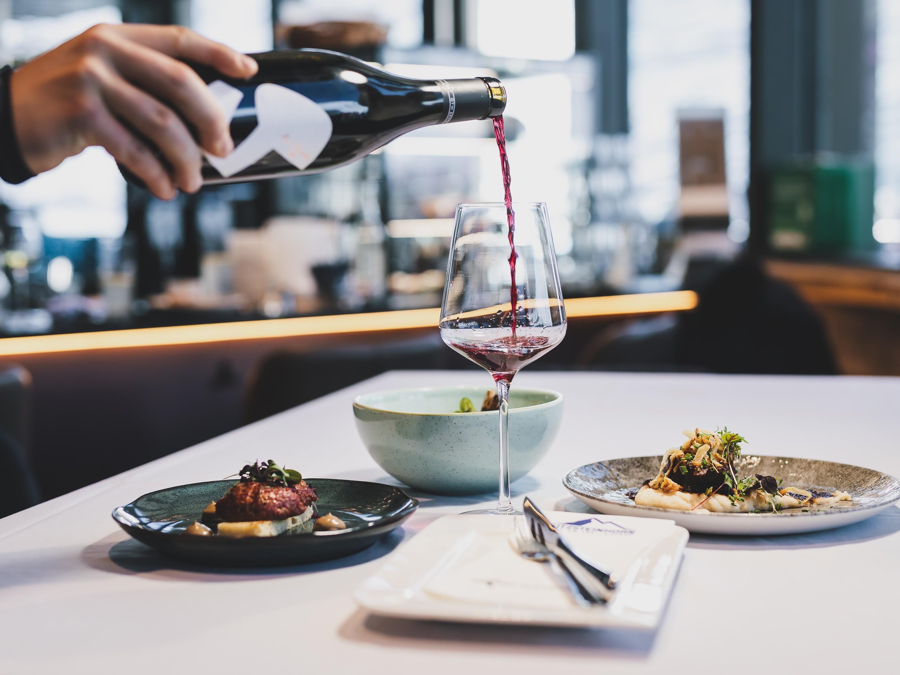 Ein eleganter Teller mit einem kunstvoll angerichteten Gericht. Im Hintergrund sind ähnliche Teller unscharf zu sehen.