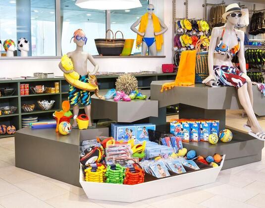 Ein farbenfrohes Geschäft mit Badebekleidung und Schwimmzubehör. Mannequins zeigen verschiedene sommerliche Outfits und Accessoires.