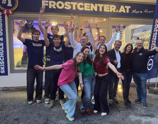 Eine Gruppe von fröhlichen Menschen steht vor einem Geschäft. Sie feiern und posieren mit erhobenen Händen.