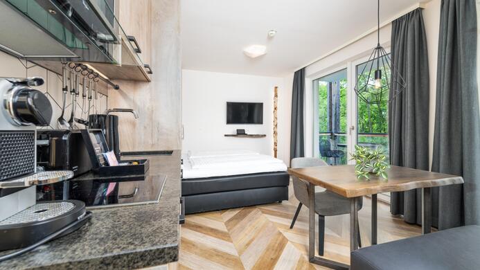 A modern kitchen unit with a dining table and a cozy sleeping nook. Large windows provide plenty of daylight and a view of the greenery.