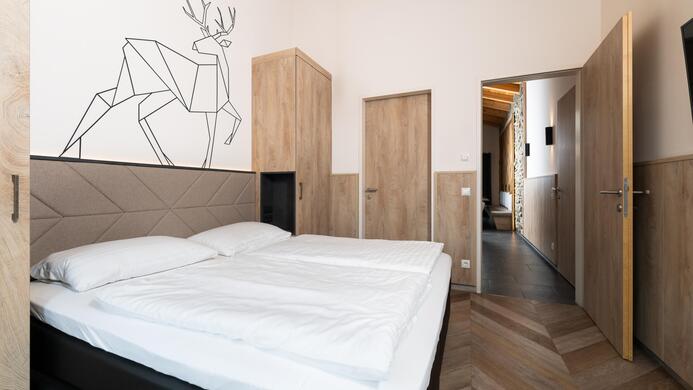 A modern room with a double bed and wooden decor. On the wall, there is a geometric ceiling drawing of a deer.