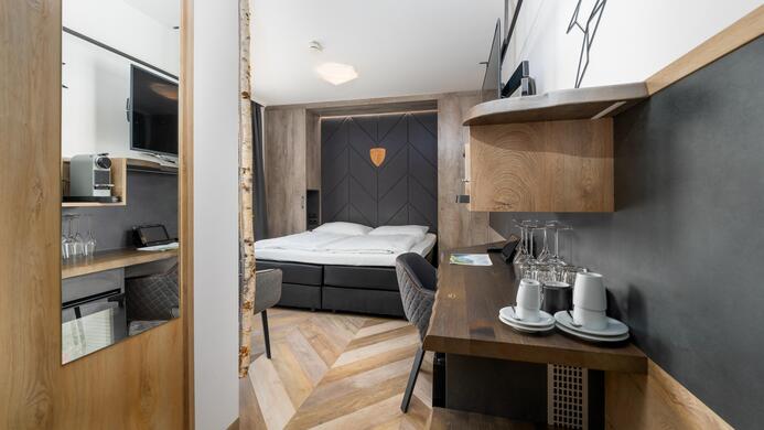 A modern hotel room with a double bed and a desk. The decor is in wood and gray tones, with a cozy atmosphere.