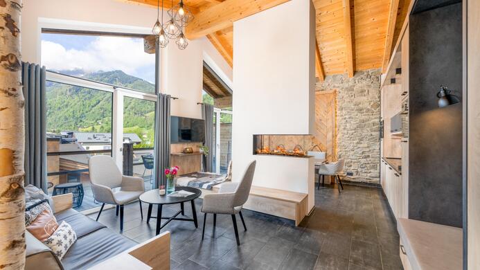 A modern living room with a wooden ceiling and large windows. There are comfortable furnishings and a beautiful view of the landscape.