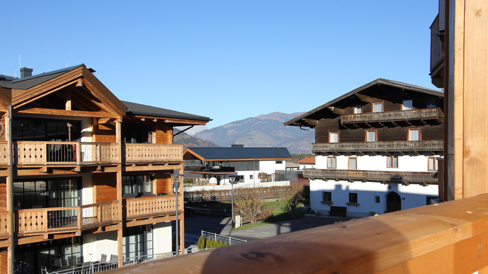 Eine alpine Landschaft mit traditionellen Holzgeb&auml;uden und einem klaren blauen Himmel. Im Hintergrund sind Berge zu sehen.