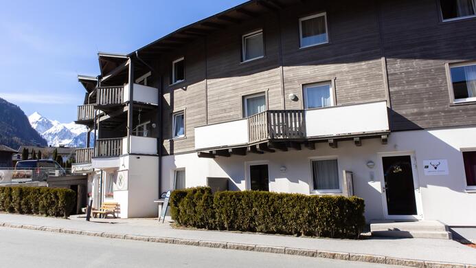 Ein modernes Haus mit mehreren Balkonen und einer sch&ouml;nen Fassade. Im Hintergrund sind schneebedeckte Berge zu sehen.