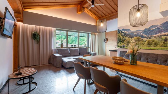 A modern living room with a wooden ceiling and large windows. The room is bright and features a cozy dining area with a table and chairs.