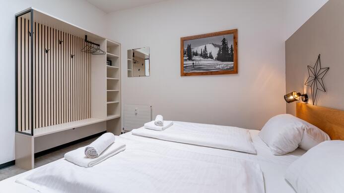 A modern bedroom with two single beds and fresh white bedding. An artwork hangs on the wall, and there is a practical wardrobe.