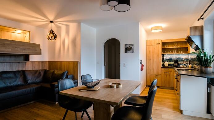 A modern kitchen with a cozy dining area and a comfortable couch. The room has a pleasant, warm atmosphere and features wood and design elements.