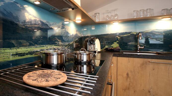 A modern kitchen with a stove and stainless steel pots. In the background, a stunning landscape photo can be seen.