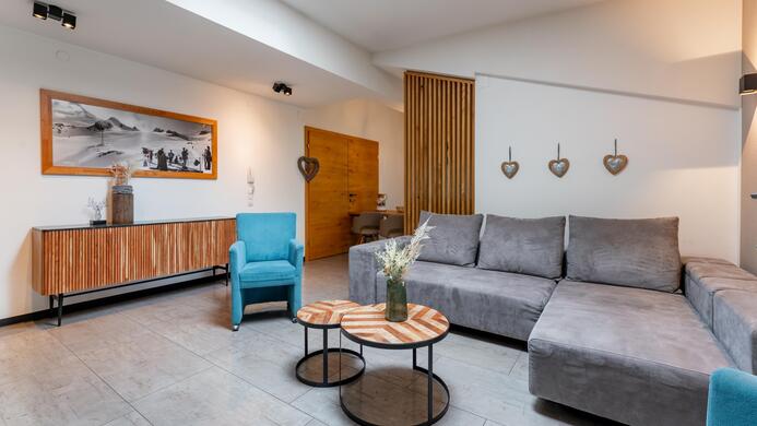 A modern living room with a gray sofa and two blue armchairs. Decorative elements and a large piece of artwork hang on the wall.