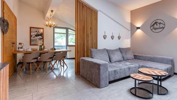 A modern living room with a gray sofa and a dining table for four people. The rooms are bright and well designed, with a warm, inviting ambiance.