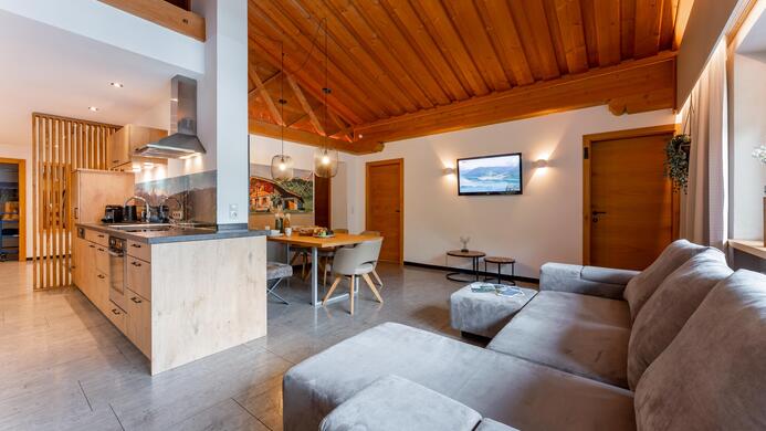 A modern apartment with a wooden ceiling and open kitchen. The living area is cozily furnished with a gray sofa and a dining area.