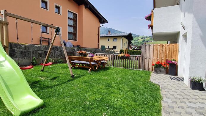 A playground in the garden with a slide and a swing. In the background, houses and mountains can be seen.