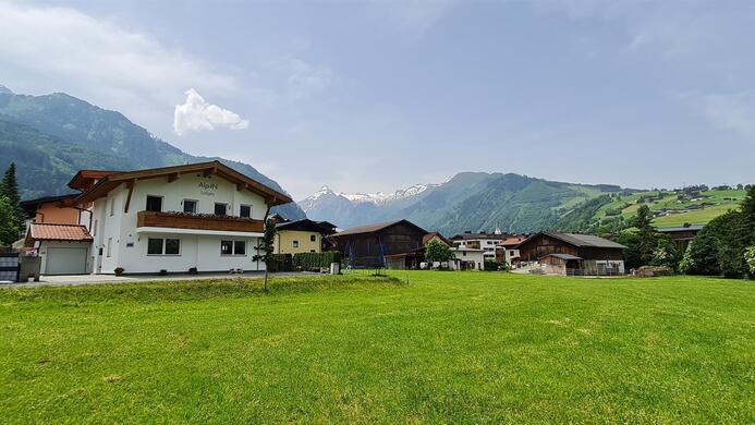 A picturesque landscape with green meadows and traditional houses. In the background, mountains and a blue sky can be seen.