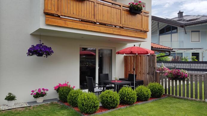 A beautifully designed garden with a terrace and a red sunshade. Blooming plants and a well-maintained lawn give the ambiance an inviting atmosphere.