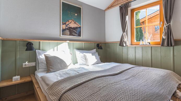 Ein gem&uuml;tliches Schlafzimmer mit einem gro&szlig;en Bett und einer warmen, einladenden Einrichtung. Das Fenster l&auml;sst viel nat&uuml;rliches Licht herein und bietet eine Aussicht auf die Umgebung.