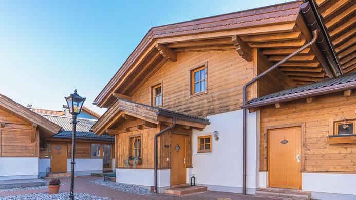 Zwei charmante Holzchalets mit einem klaren blauen Himmel. Der Bereich ist mit Kies und einem Laternenpfahl gestaltet.