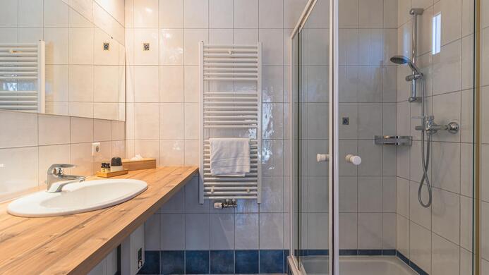 Ein modernes Badezimmer mit einer Dusche und einem gro&szlig;en Waschbecken. Die W&auml;nde sind fliesenverkleidet und es gibt einen Handtuchtrockner.