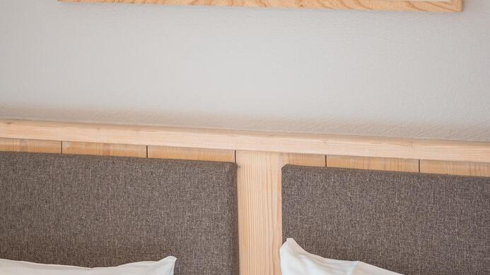 Ein gem&uuml;tliches Schlafzimmer mit einem Holzbettrahmen. &Uuml;ber dem Bett h&auml;ngt ein Bild eines Hochlandrinds.