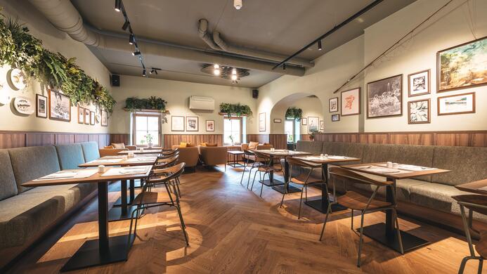 Ein modern gestaltetes Restaurant mit bequemen Sitzgelegenheiten und Holztischen. Die W&auml;nde sind mit Bildern verziert, und Pflanzen sorgen f&uuml;r eine angenehme Atmosph&auml;re.