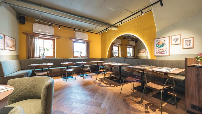Ein modernes Restaurant mit hellen W&auml;nden und einem gem&uuml;tlichen Ambiente. Die Tische und St&uuml;hle sind ordentlich angeordnet und warten auf G&auml;ste.
