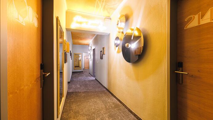 Ein heller Hotelflur mit modernen T&uuml;ren und dekorativen Wandinstallationen. Die Beleuchtung verleiht dem Raum eine einladende Atmosph&auml;re.