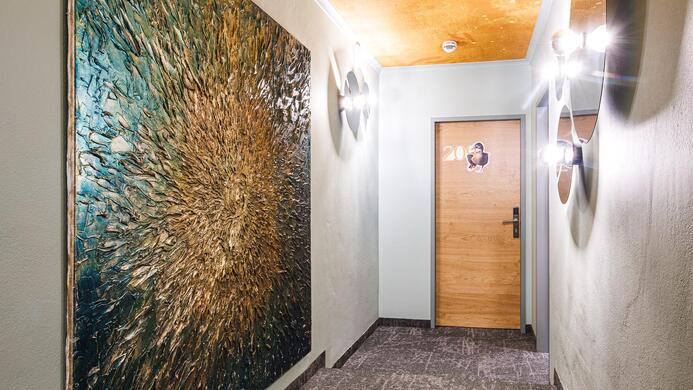 Ein eleganter Flur mit einem gro&szlig;en Kunstwerk an der Wand. Die Decke hat eine warme Farbgebung und die Beleuchtung schafft eine einladende Atmosph&auml;re.