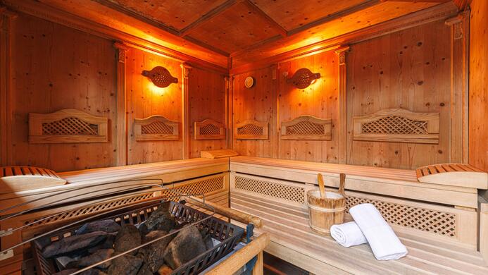 Eine gem&uuml;tliche Sauna mit Holzverkleidung und sanfter Beleuchtung. Im Inneren befinden sich Handt&uuml;cher und ein Eimer f&uuml;r Wasser.
