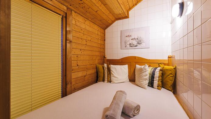 Ein gem&uuml;tliches Schlafzimmer mit Holzw&auml;nden und einem gro&szlig;en Bett. Auf dem Bett liegen Kissen und Handt&uuml;cher.