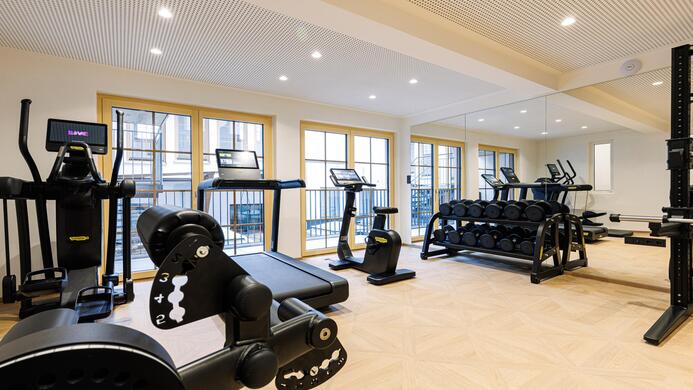 Ein modernes Fitnessstudio mit verschiedenen Trainingsger&auml;ten. Gro&szlig;e Fenster sorgen f&uuml;r viel Tageslicht.