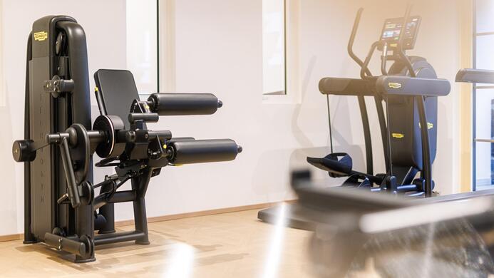 Ein modernes Fitnessstudio mit verschiedenen Trainingsger&auml;ten. Im Vordergrund ist eine Beinpresse und im Hintergrund ein Crosstrainer zu sehen.