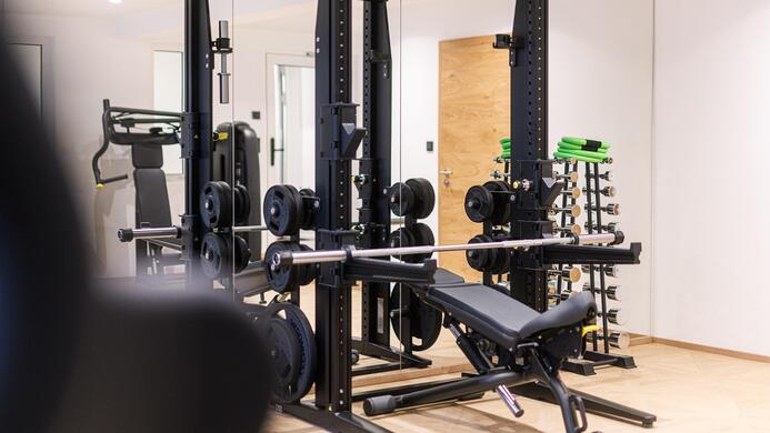 Ein gut ausgestatteter Fitnessraum mit Krafttrainingsger&auml;ten und Spiegeln. Die Umgebung ist modern und hell.
