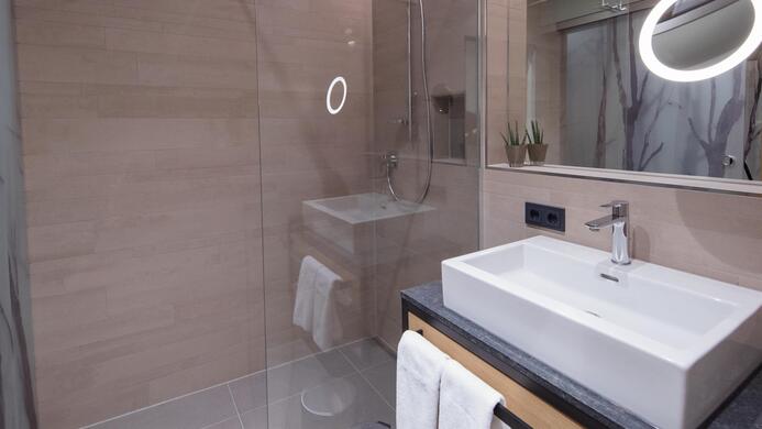A modern bathroom with a glass shower and an elegant sink. The walls are painted in neutral tones, and there is stylish lighting.
