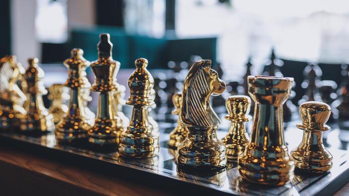 A chessboard with shiny, golden pieces. The chess pieces are standing on a black background.