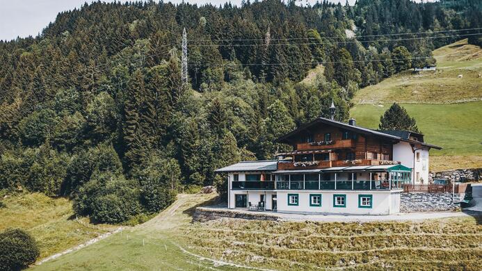 Ein charmantes Alpenhaus umgeben von &uuml;ppigem Gr&uuml;n und B&auml;umen. Der Blick auf die sanften H&uuml;gel ist malerisch und einladend.
