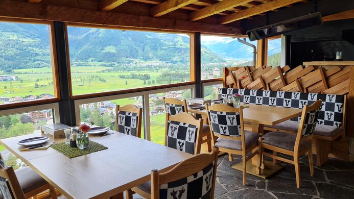 Ein gem&uuml;tliches Restaurant mit Holzdekor und Aussicht auf eine gr&uuml;ne Landschaft. Die Tische sind elegant gedeckt und die St&uuml;hle haben ein einzigartiges Muster.