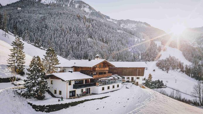 Ein charmantes Geb&auml;ude inmitten einer schneebedeckten Landschaft. Die Sonne geht hinter den Bergen auf und taucht die Szenerie in warmes Licht.