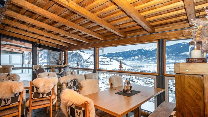 Ein gem&uuml;tlicher Restaurantbereich mit Holzdekor und Schafsfellsesseln. Gro&szlig;e Fenster bieten einen Blick auf die schneebedeckte Landschaft.