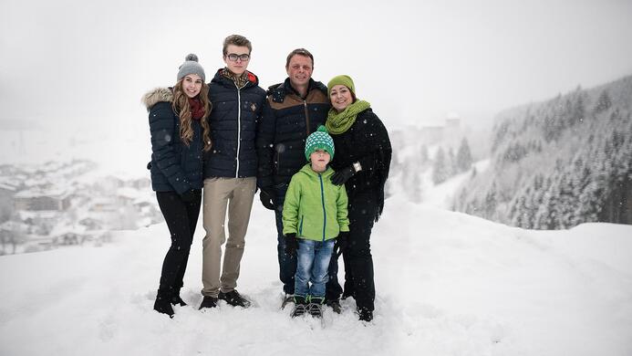 Eine Gruppe von f&uuml;nf Personen steht in einer verschneiten Landschaft. Sie tragen winterliche Kleidung und l&auml;cheln in die Kamera.