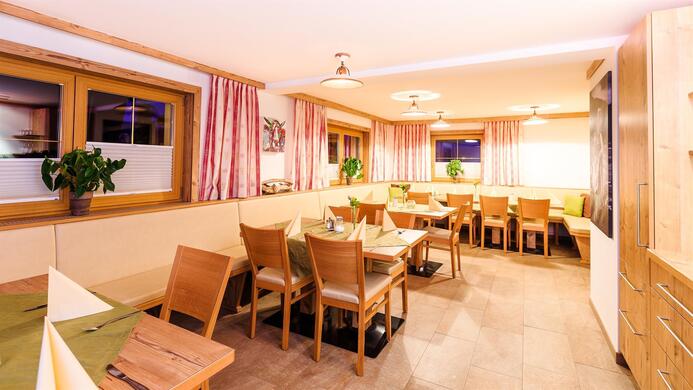 Ein gem&uuml;tliches Restaurant mit Holzst&uuml;hlen und Tischen. Sanftes Licht und dekorative Pflanzen schaffen eine einladende Atmosph&auml;re.