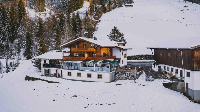 Eine gem&uuml;tliche Bergh&uuml;tte im Schnee, umgeben von Nadelb&auml;umen. Die Landschaft ist winterlich und einladend.