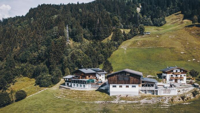 Eine malerische Berglandschaft mit mehreren gem&uuml;tlichen Chalets. Die Umgebung ist gr&uuml;n und bewaldet, ideal f&uuml;r einen entspannten Urlaub.