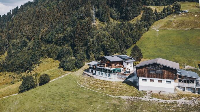 Ein malerisches Geb&auml;ude inmitten von gr&uuml;nen Wiesen und W&auml;ldern. Die Umgebung zeigt eine ruhige, bergige Landschaft.