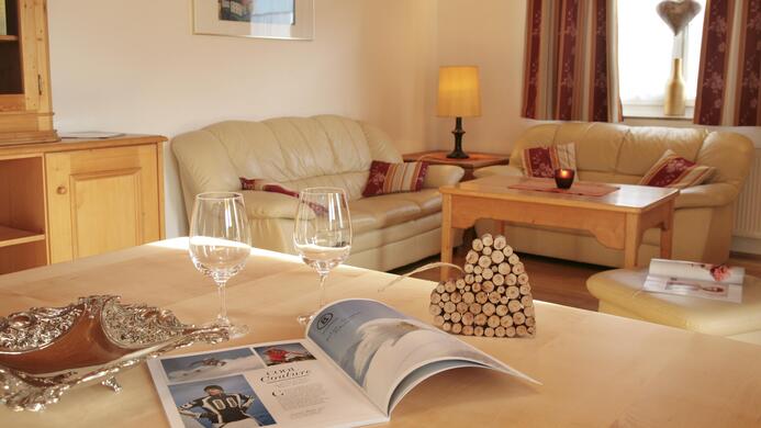 Ein gem&uuml;tliches Wohnzimmer mit hellen Sofas und einem Holztisch. Auf dem Tisch liegen Zeitschriften und ein dekoratives Herz aus Kork.